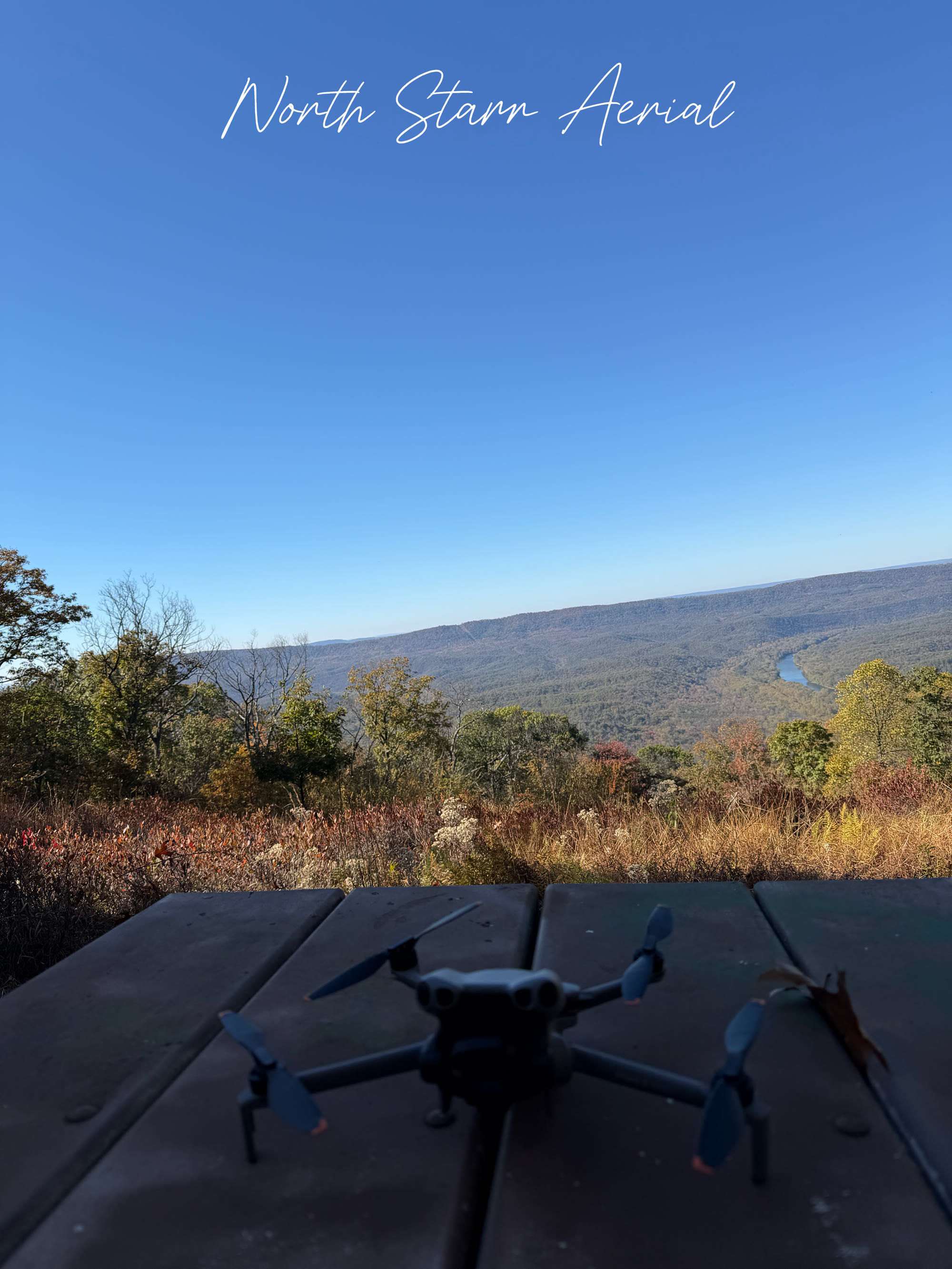 DJI Mini drone on a picnic table overlooking a fall river valley, with North Starr Aerial script at the top